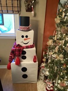 a snowman made out of cardboard sitting next to a christmas tree