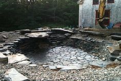 an outdoor fire pit made out of rocks and stones in front of a house with construction equipment around it