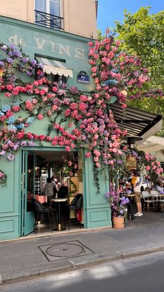 the outside of a restaurant with pink flowers growing on it's side and people sitting at tables in front