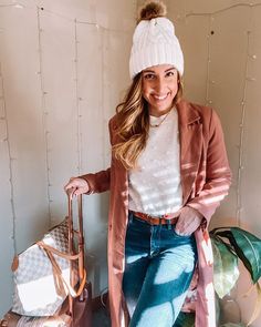 a woman sitting on top of a suitcase next to a pile of luggage wearing a white beanie