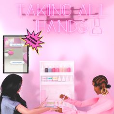 two women sitting at a table in front of a pink neon sign that says taking all hands