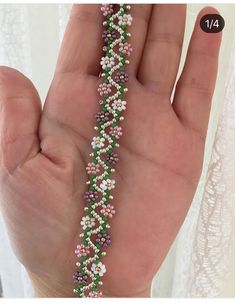 a hand holding a beaded bracelet with flowers on it