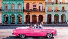 an old pink car parked in front of colorful buildings