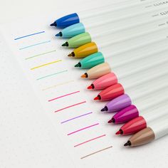 several different colored pencils lined up on top of a white paper with lines in the middle