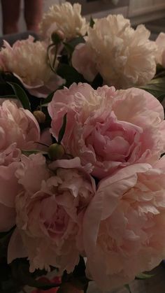 pink peonies are arranged in a vase on the counter top, with green leaves