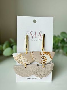 two earrings with gold and white designs on them, sitting in front of a card