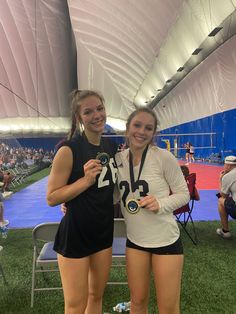 two women standing next to each other holding medals in front of a tent filled with people