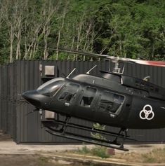 a black helicopter is parked in front of a building with trees on the other side