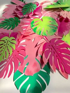 a bunch of cut out paper flowers sitting on top of a white table with green and pink leaves