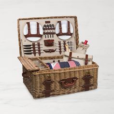 an open wicker picnic basket with utensils and other items in it on a marble surface