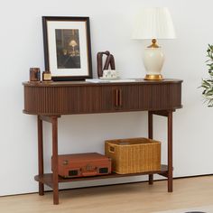 a wooden table with a lamp and suitcase on it next to a white wall in a living room