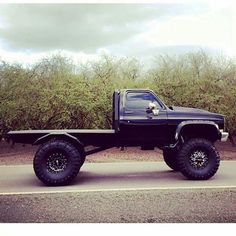 a large black truck parked on the side of a road with trees in the background