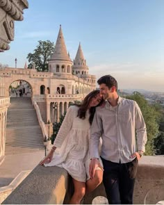 a man and woman standing next to each other in front of a castle