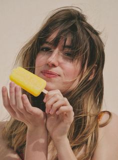 a woman with long hair is holding a piece of food in her hand and looking at the camera