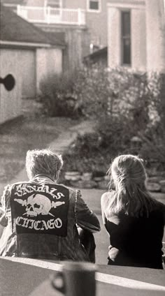 black and white photograph of two people sitting on a bench in front of a house