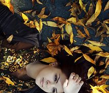 a woman laying on the ground surrounded by yellow and brown leaves with her eyes closed