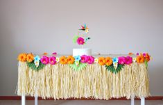 a table topped with a white cake covered in flowers and grass next to a wall