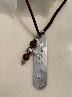 Custom Braille Necklace.   Braille is done by hand with a Slate & Stylus.  There are 7 braille cells available  (including the capital sign) and if there are more letters and can fit into 7 cells contracted Braille can be used.   The tag is aluminum and does not tarnish.   The tag hangs on a leather cord along with a colored bead/jewel.  You may choose the name or letters on the Braille tag and also the color for the accent beads/stones/jewels. Since the Braille is done on a Slate & Stylus; it i Braille Necklace, Viking Ideas, Braille Jewelry, Name Necklaces, Beaded Jewels, The Capital, A Plus, Jewelry Bags, Stylus