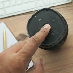 a hand is pressing the button on a wireless speaker next to a keyboard and mouse