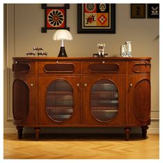 a large wooden cabinet with glass doors on the top and bottom, in front of a wall with pictures above it