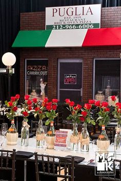 a bunch of vases filled with red roses on top of a table in front of a restaurant