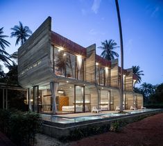 a modern house is lit up at night with palm trees in the foreground and an ocean view behind it