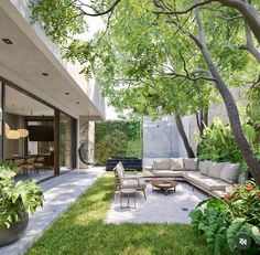 an outdoor living area with couches, tables and chairs in the grass next to trees