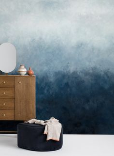 a room with a dresser, mirror and blue ombretta wallpaper on the walls