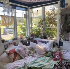 a bedroom with lots of pillows and stuffed animals on the bed in front of large windows