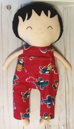 a doll with black hair wearing red overalls