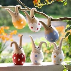 several ceramic cats are hanging from a tree branch with flowers in the back ground behind them