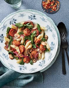 pasta with sausage and spinach in a white bowl on a blue table cloth next to a glass of water