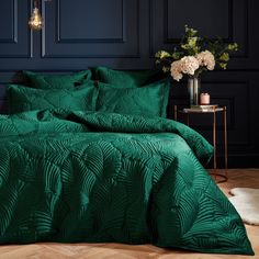 a bed with green comforter and pillows in a dark room next to a table