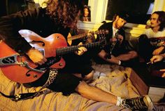 a group of people sitting on top of a bed with guitars in front of them