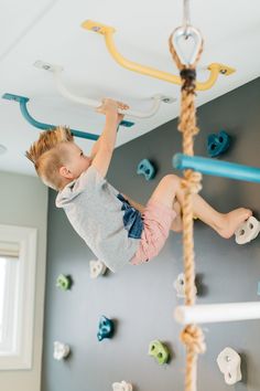 a young boy climbing on a rope in a play room with blue and white walls