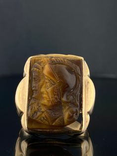 Super cool vintage Mid Century Intaglio Carved ring with Centurions.  It is very unusual to carve Tiger's eye in this fashion. Tiger's eye crystal holds a rich history dating back centuries. It was used by ancient civilizations like the Egyptians and Romans for its beauty and metaphysical properties. It was carved into amulets and jewelry in Egypt, symbolizing divine vision and protection. It was carried as a talisman in Roman times to boost bravery and enhance focus. This ring evokes the Roman era with it's carved soldiers. The tiger's eye has a chip in one of the corners, please note in the photos.  The resurgence of modern signet rings will put you in a class of your own with this vintage piece.   Materials: 10 Karat yellow Gold (Hallmarked "10k" and "Hand Made", Acid tested for purity) Roman Era, Tiger Eye Crystal, Carved Ring, Egyptian Jewelry, Signet Rings, Gold Signet Ring, Tiger Eye Stone, Amulets, Tiger's Eye