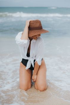 a woman sitting on the beach wearing a hat