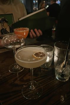 two martinis sitting on top of a wooden table next to glasses filled with drinks