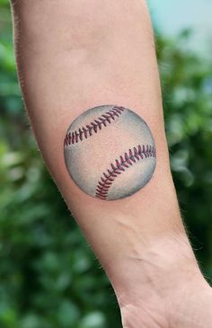 a baseball tattoo on the arm of a person's left hand, with trees in the background