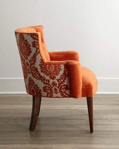 an orange chair sitting on top of a hard wood floor next to a white wall