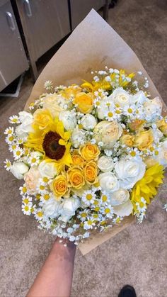 a bouquet of sunflowers and daisies is being held by someone's hand