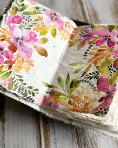 an open book with flowers on it sitting on a wooden table