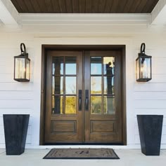 two black planters on the side of a white house with wooden doors and windows