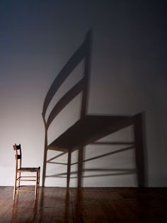 the shadow of a chair and a wooden chair on a wood floor in front of a white wall