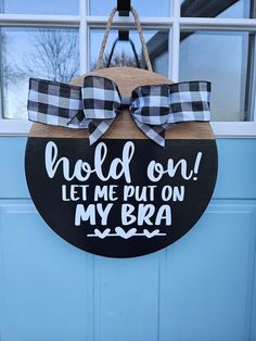 a black and white sign that says hold on let me put on my bra hanging from a door