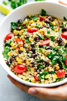 a person holding a white bowl filled with vegetables and couscouse on top of a table