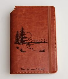 a brown leather journal with the words the second half written on it and trees in the background