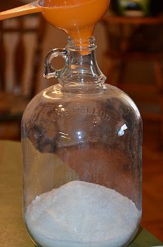 a glass bottle filled with white sand on top of a wooden table next to an orange drink