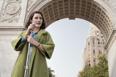 a woman in a green coat is holding a crutch and standing under an arch