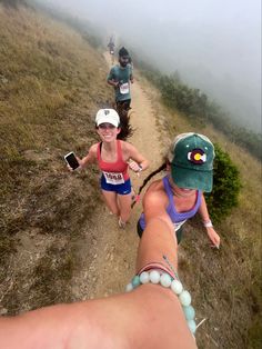 three people are running on a trail in the foggy mountains, one is holding her hand out